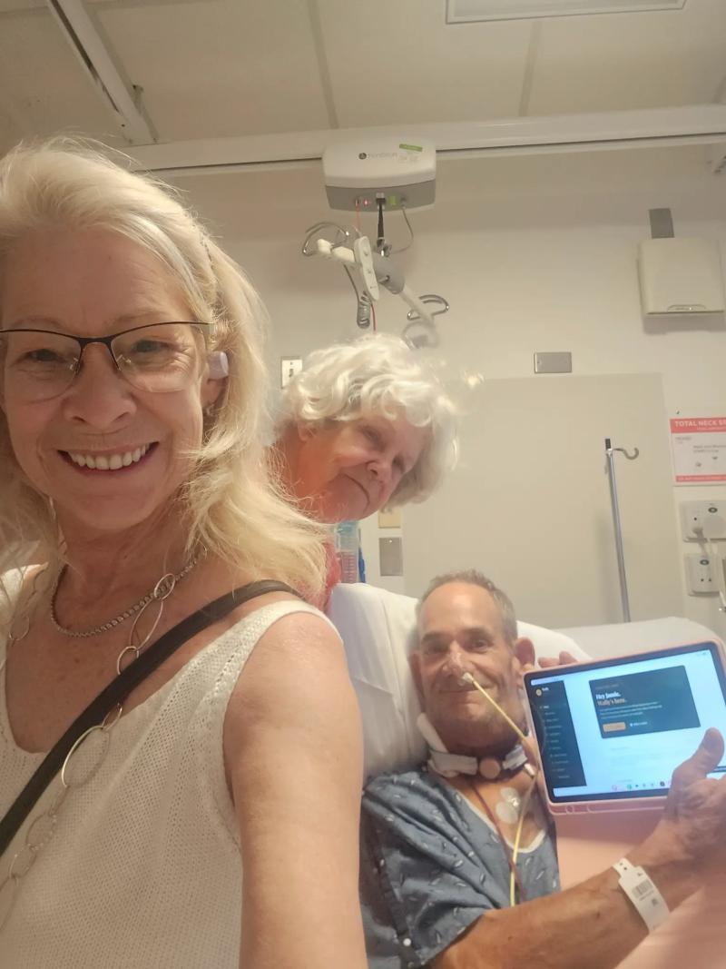 Amy and her mother beside Jamie in his hospital bed as he holds Wally on a tablet