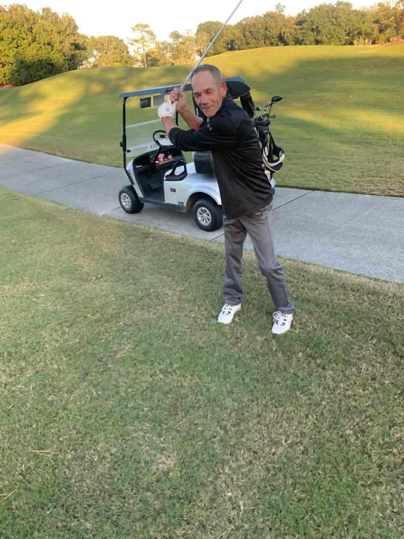 Jamie standing beside a golf cart and taking a practice swing on the course
